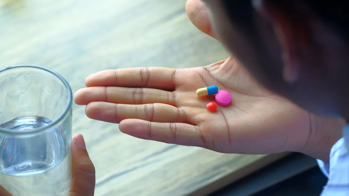 A man holding three different pills in his palm next to a glass of water