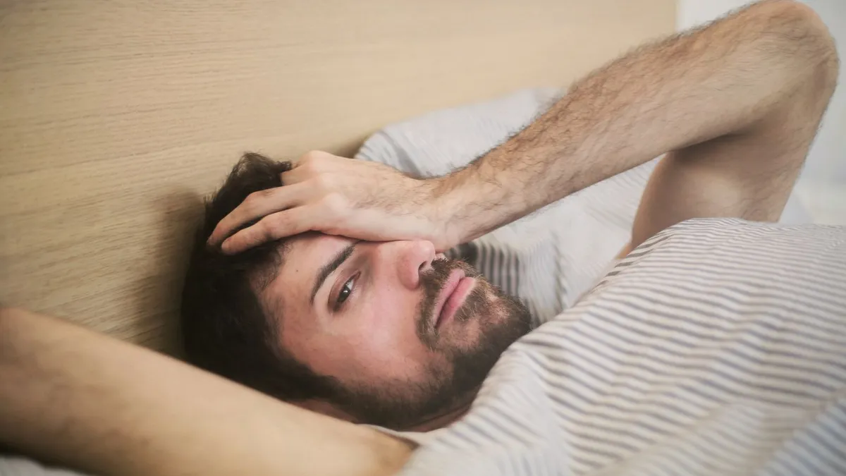 A tired man lying in bed in the morning with his hand on his forehead